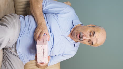 Vertical-video-of-Old-man-opening-gift-box-at-home-excited-and-happy.