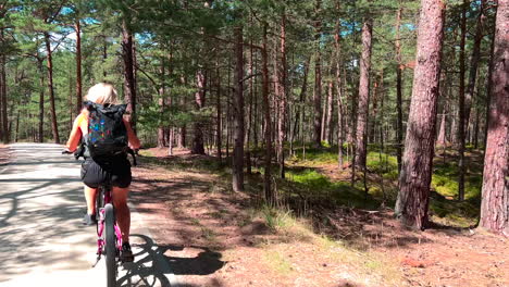 mujer joven montando en bicicleta en el parque de la ciudad de verano, bosque de coníferas - cámara lenta
