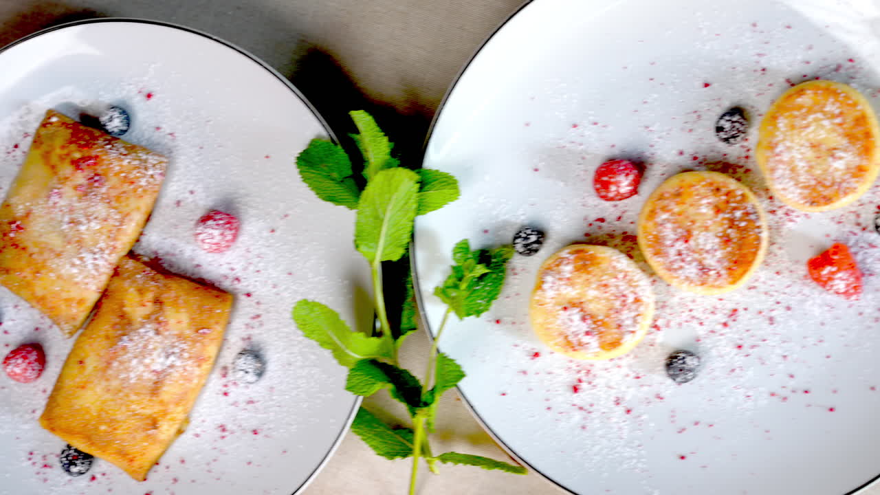 Colazione tradizionale dell'Europa orientale con syrniki e nalysnyky servita con frutti di bosco freschi, menta e zucchero a velo su piatti bianchi, accompagnata da posate su un tavolo