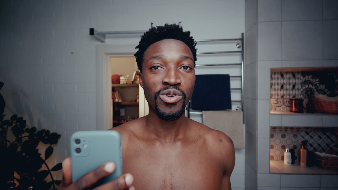 blogger masculino negro grabándose a sí mismo con un teléfono inteligente en el baño