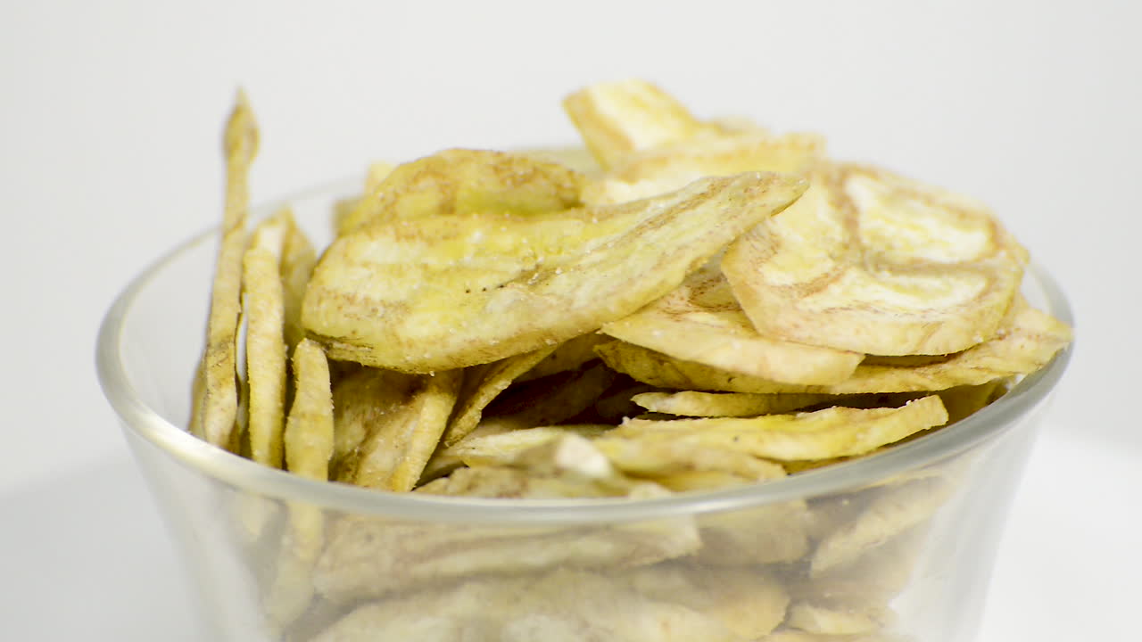 Detail of banana chips in a glass jar rotating on a white background