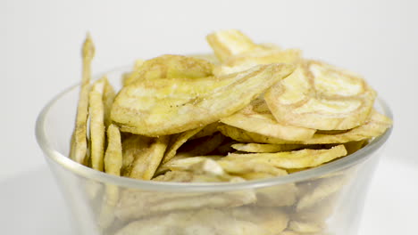 detalle de chips de plátano en un frasco de vidrio girando sobre un fondo blanco