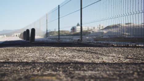 Legs-of-person-running-on-path-by-wire-fence-and-beach-on-sunny-day