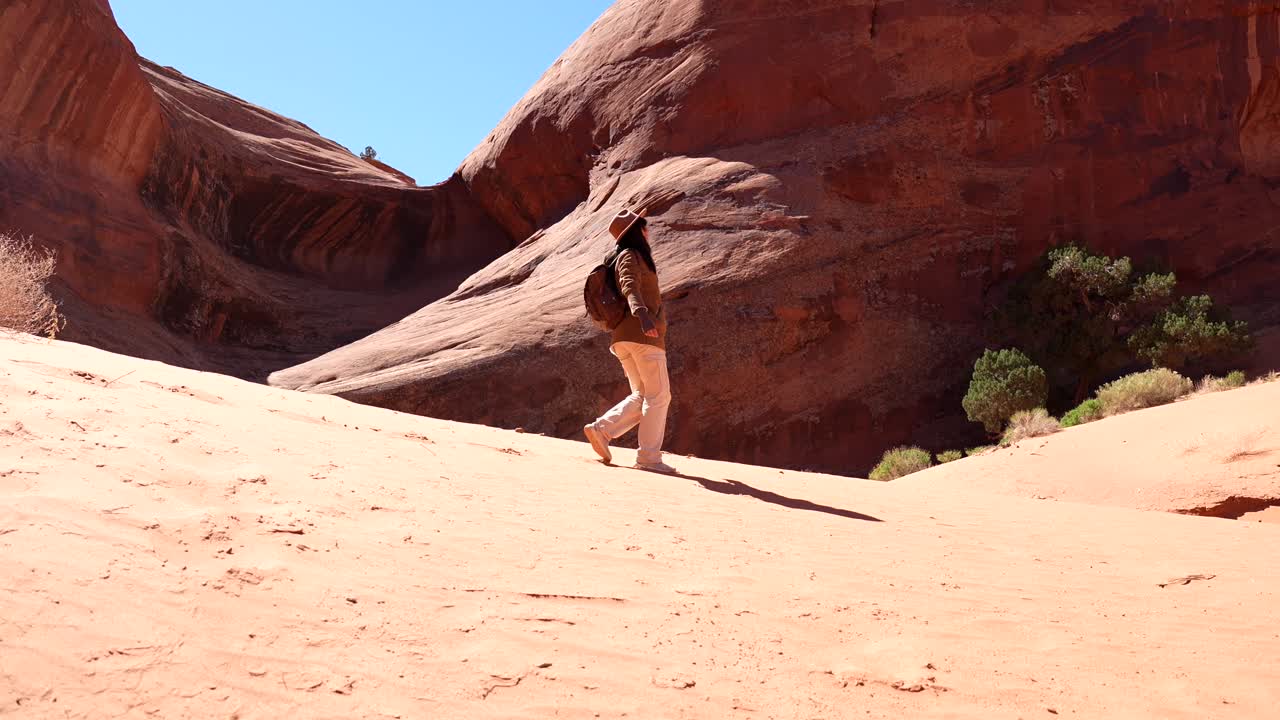 Donna che fa escursioni attraverso un canyon desertico sabbioso con formazioni rocciose rosse