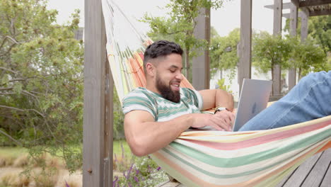 relaxing in hammock, man using laptop and smiling in outdoor setting