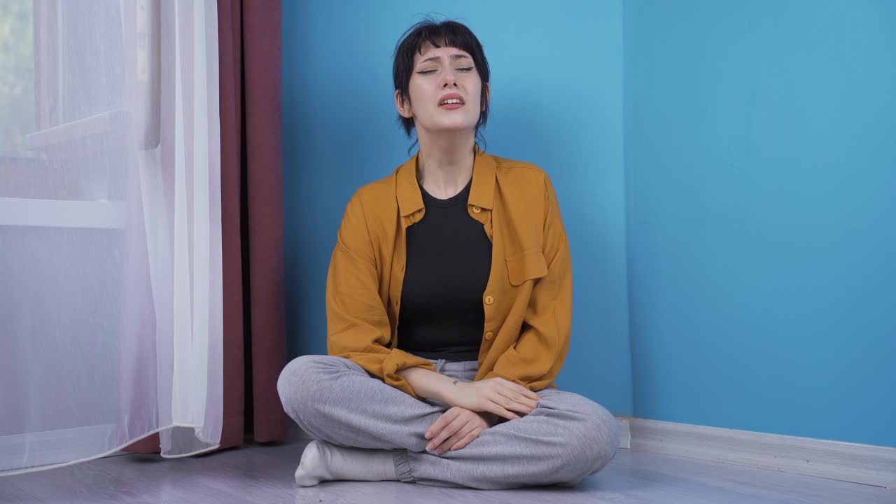 바닥에 앉아 있는 젊은 여성은 울고 있습니다. 절망적입니다.