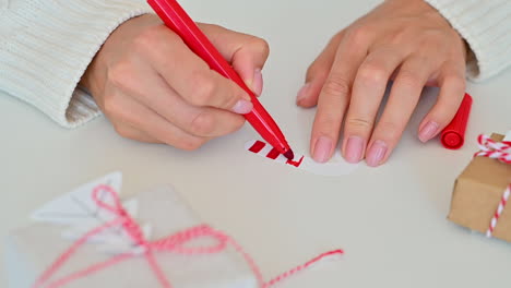 female hands decorate the bow of a wrapped christmas gift with a paper tree