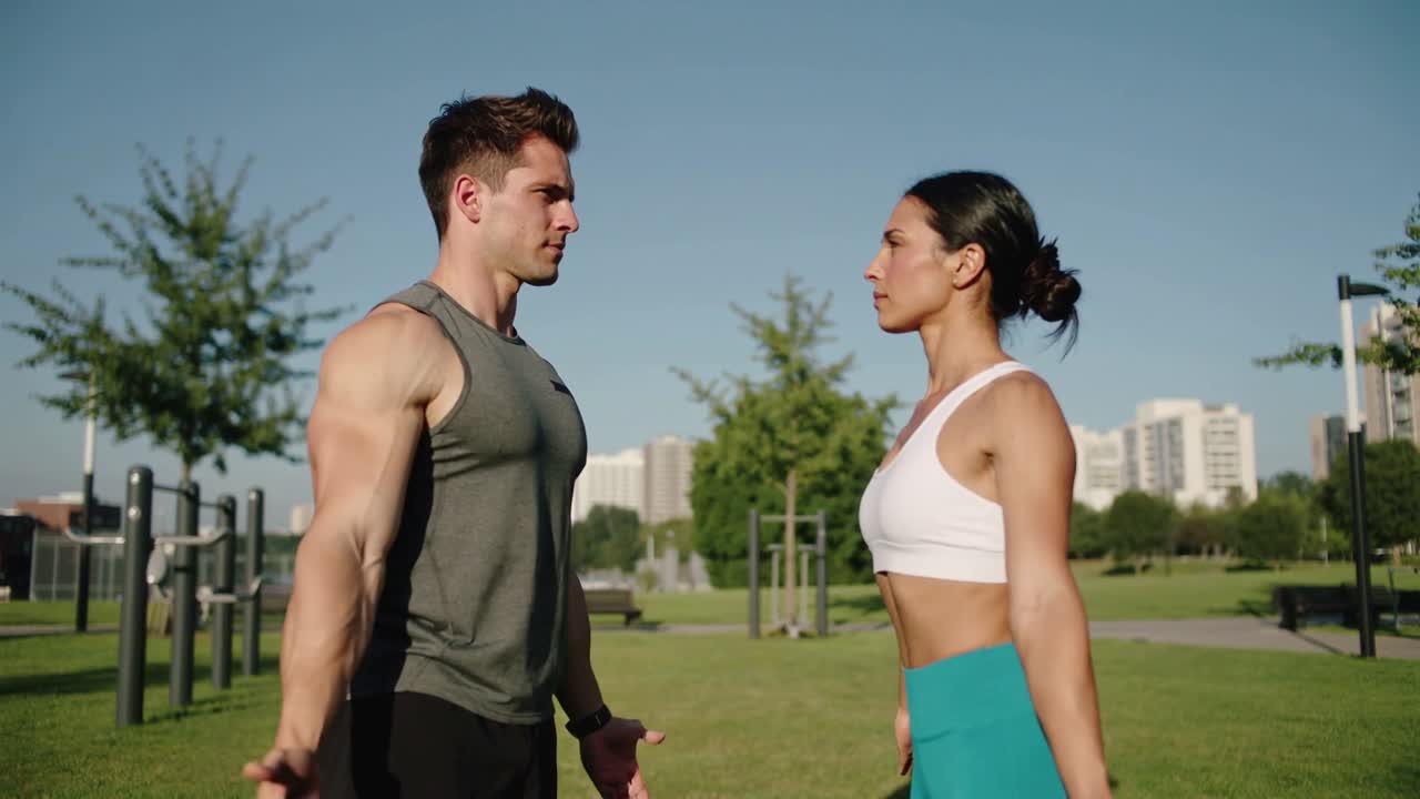 En mand i grå tanktop og en kvinde i hvid sports-bh udfører synkroniserede armløft ved parkens træningsstænger.