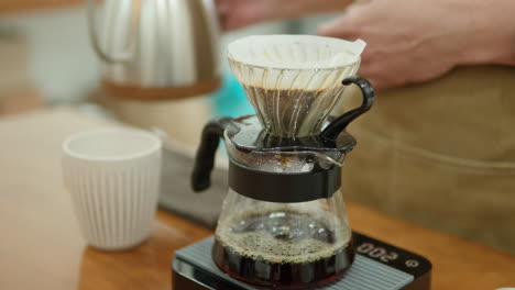 barista brewing hand drip coffee - man's hands pouring hot water from drip kettle into coffee dripper on drip scale