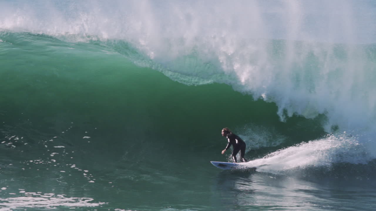 Surfer locks into emerald green barrel before wave crashes in cascade of foam