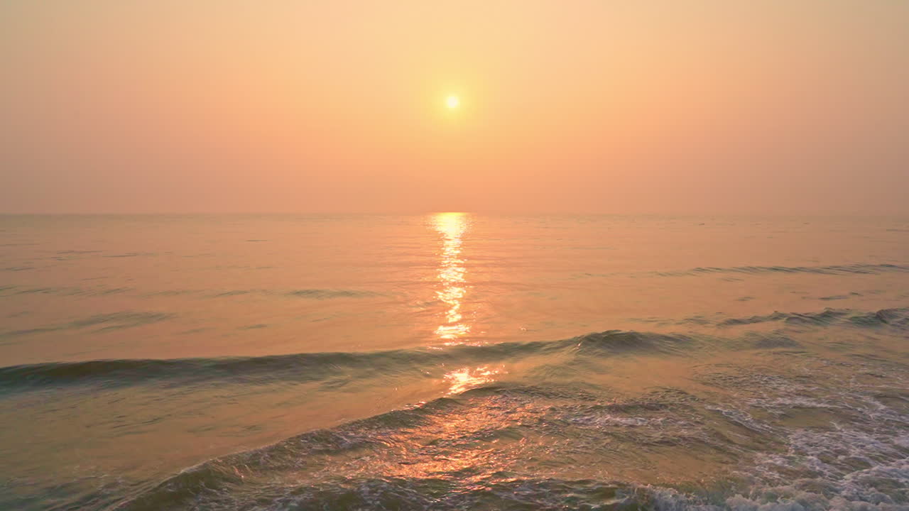 Pan across a pink, orange and yellow sunset while waves crash along the shore below