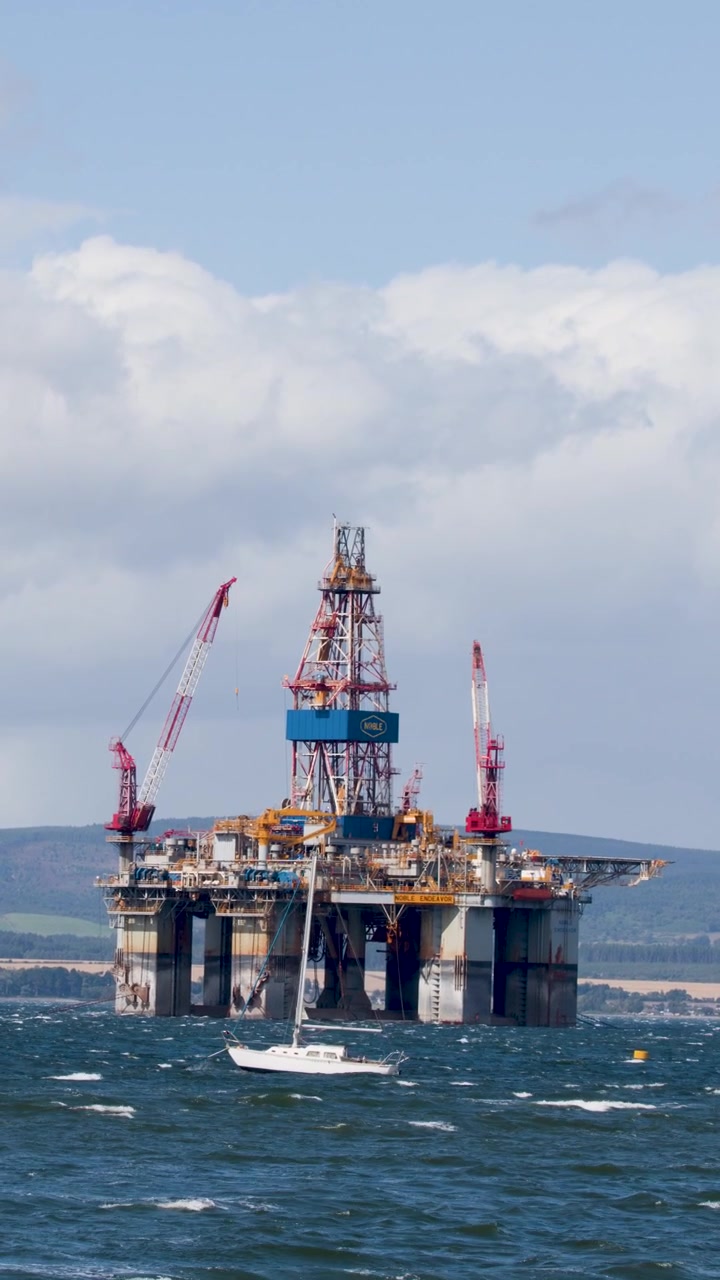 Offshore olieplatform og passerende yacht i dagslys, vidvinkelbillede, stabilt kamera, delvist skyet himmel.