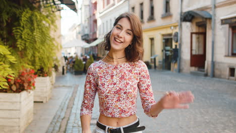 mujer joven sonriendo amigablemente a la cámara, agitando las manos hola, hola, saludo o adiós en la calle de la ciudad
