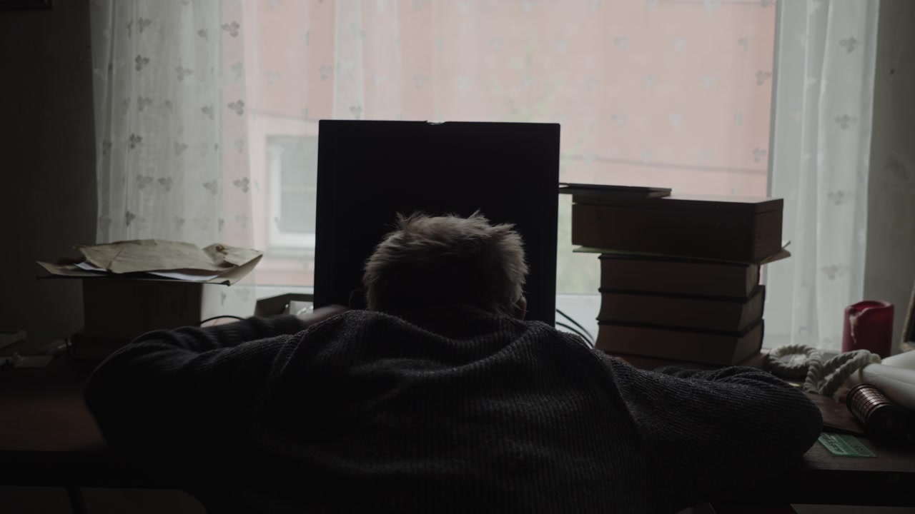 Backlit scene of an exhausted home worker collapsed over a keyboard, highlighting burnout, overwork, and the emotional toll of relentless deadlines.