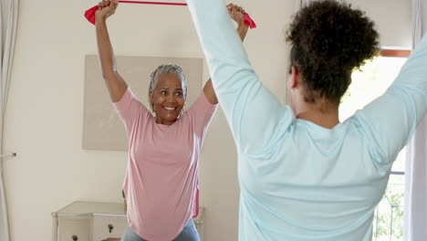 senior woman exercising with resistance band, guided by carer at home