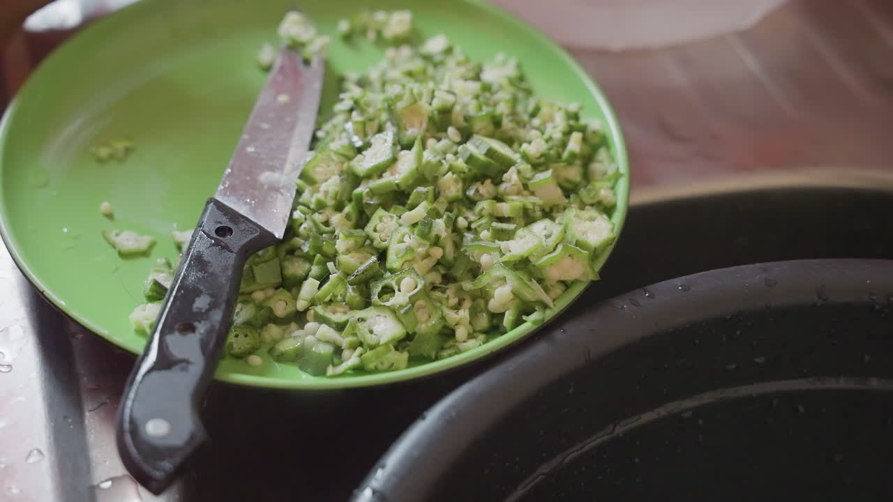 Closeup green plate chopped peas, knife resting at edge, pepper specks and coarse texture visible, stainless sink rim in frame, steady hands moving bowl, quick focused seasoning and plating