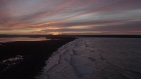 predawn sunrise colour on sea coast, waves gently roll onto dark beach