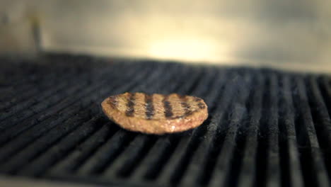 Hamburger-patty-grilling-on-BBQ-with-charcoal-marks,-Closeup-Macro-Shot