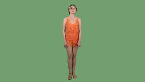 portrait of a beautiful young woman looking straight and smiling. pretty brunette in an orange fringed dress on a green screen in the studio. slow motion