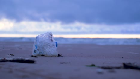 Empty-plastic-bottle,-trash-and-waste-litter-on-an-empty-Baltic-sea-white-sand-beach,-environmental-pollution-problem,-overcast-evening-after-sunset,-closeup-shot