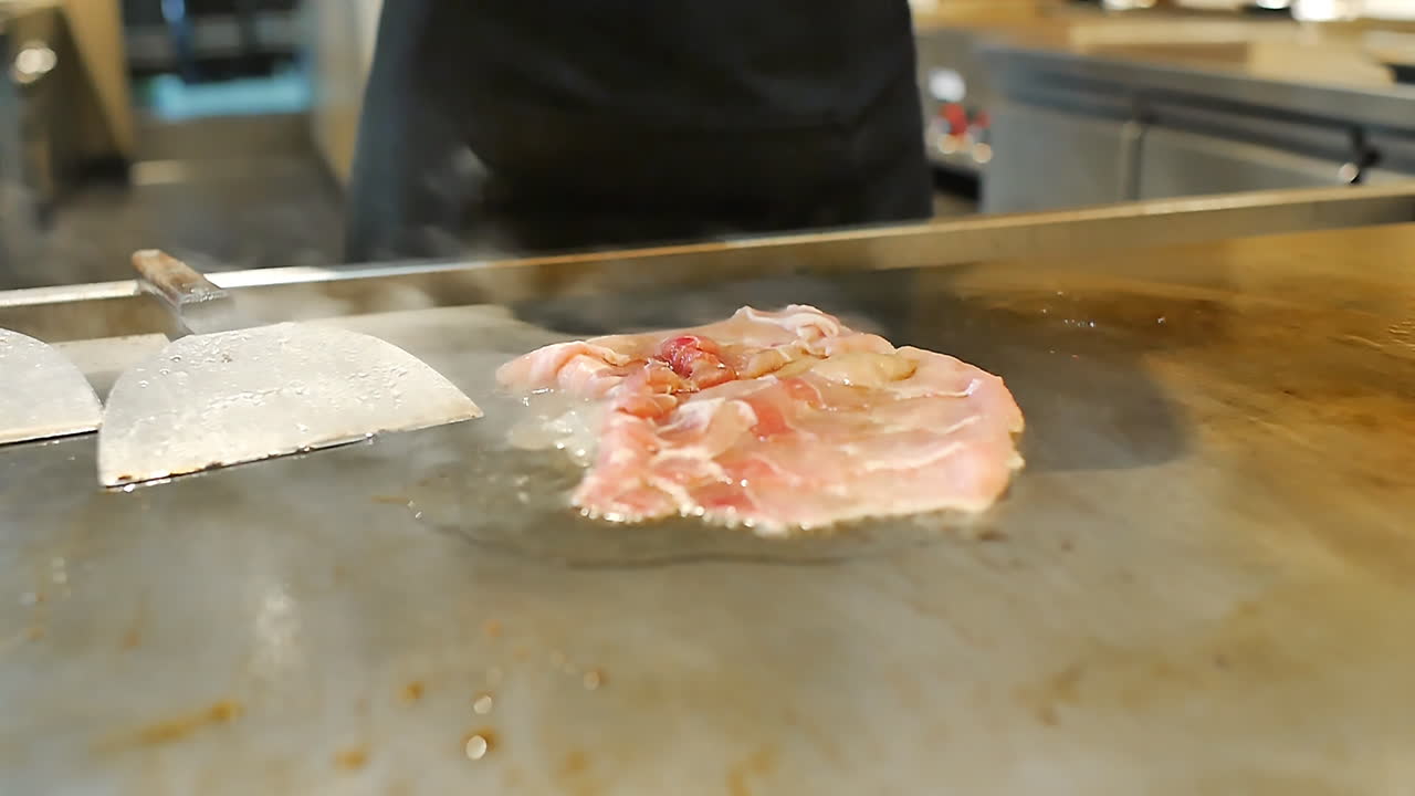 Close-up of a skilled chef preparing teppanyaki Japanese cuisine on a hot iron griddle in front of guests, grilling fresh ingredients with flair. Perfect for Japanese food culture and live cooking