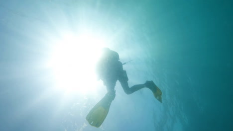 scuba diver ascending directly to surface and fading into reflection of sunlight