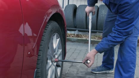 car mechanic screwing or unscrewing car wheel of lifted automobile at repair service station