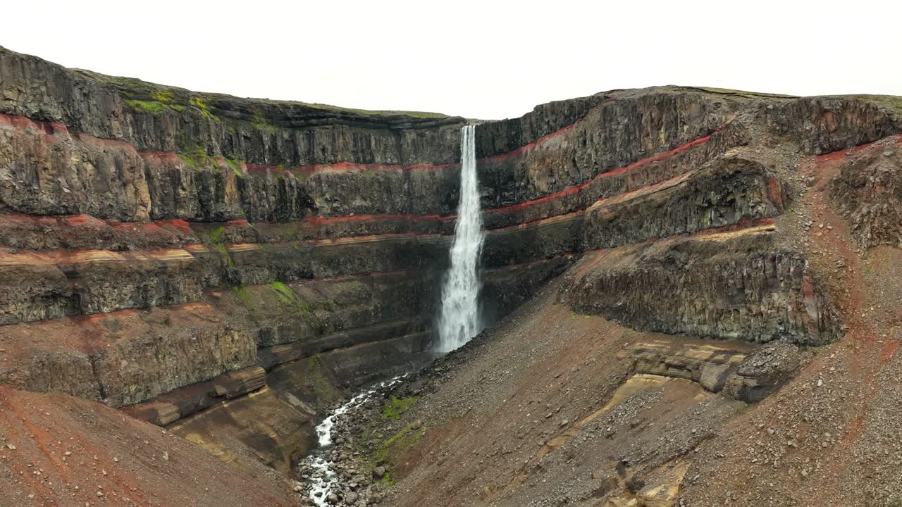 Aerial establishing shot of crashing Hengifoss Waterfall down volcanic hills. Flowing rocks stream on island info iceland at fall season