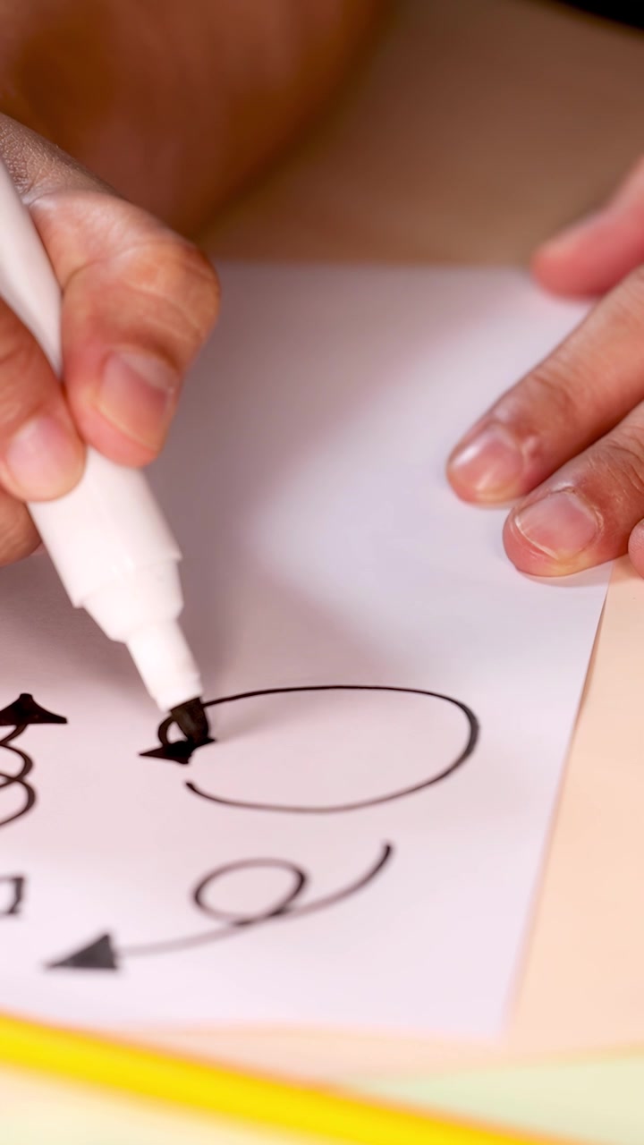 Primo piano di una mano che disegna frecce e scarabocchi creativi su carta bianca con un pennarello, illuminazione naturale.