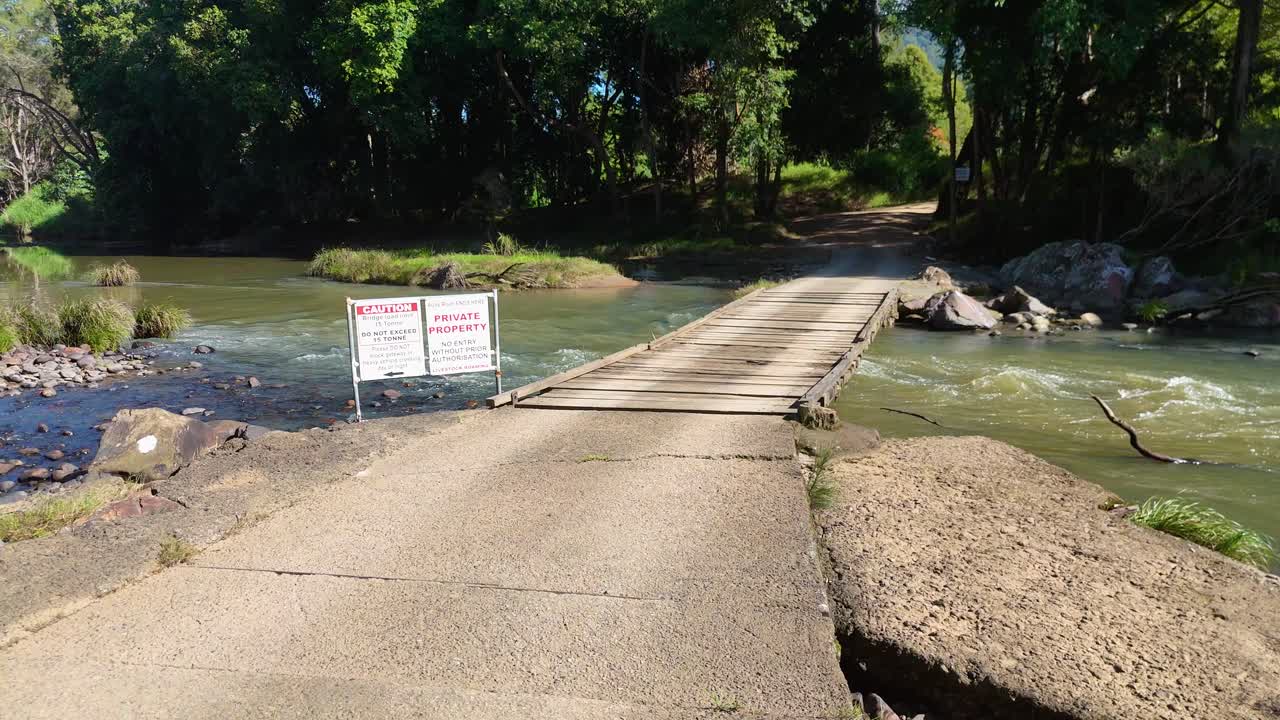 A small bridge over a creek with a private property sign, surrounded by lush greenery and bright daylight
