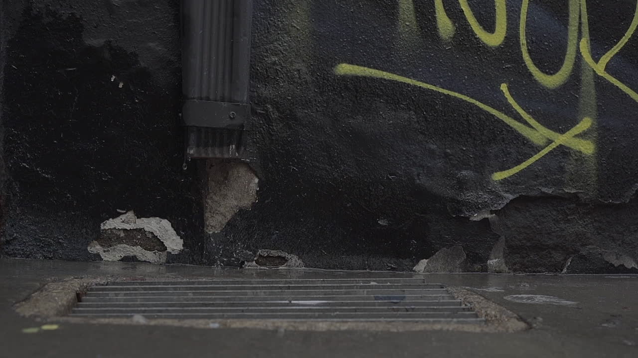 Cinematic Slow Motion shot of rain drops on urban downtown streets with black graffiti wall