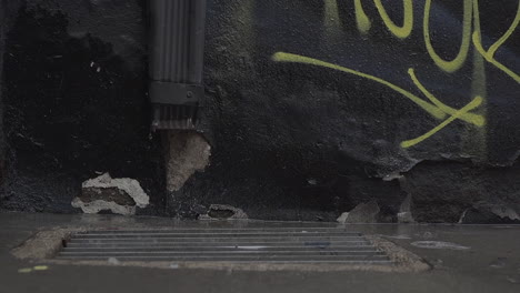 cinematic slow motion shot of rain drops on urban downtown streets with black graffiti wall