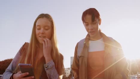 front view of a caucasian and a mixed race girl walking and using their phone