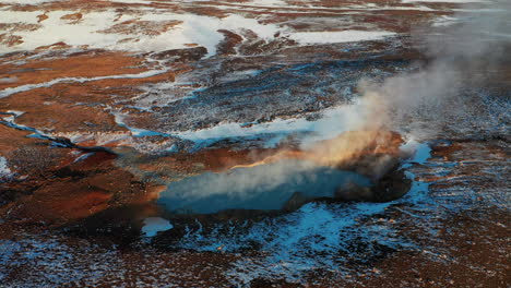 geothermal steam rising above the blue lake in volcanic lava field - south iceland - aerial drone shot