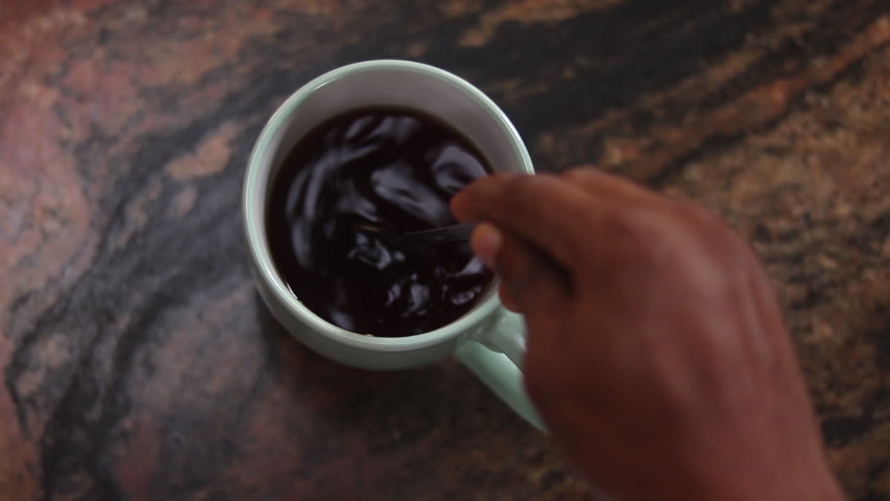 Long high angle view of hand stirring in cup of hot tea and removing spoon