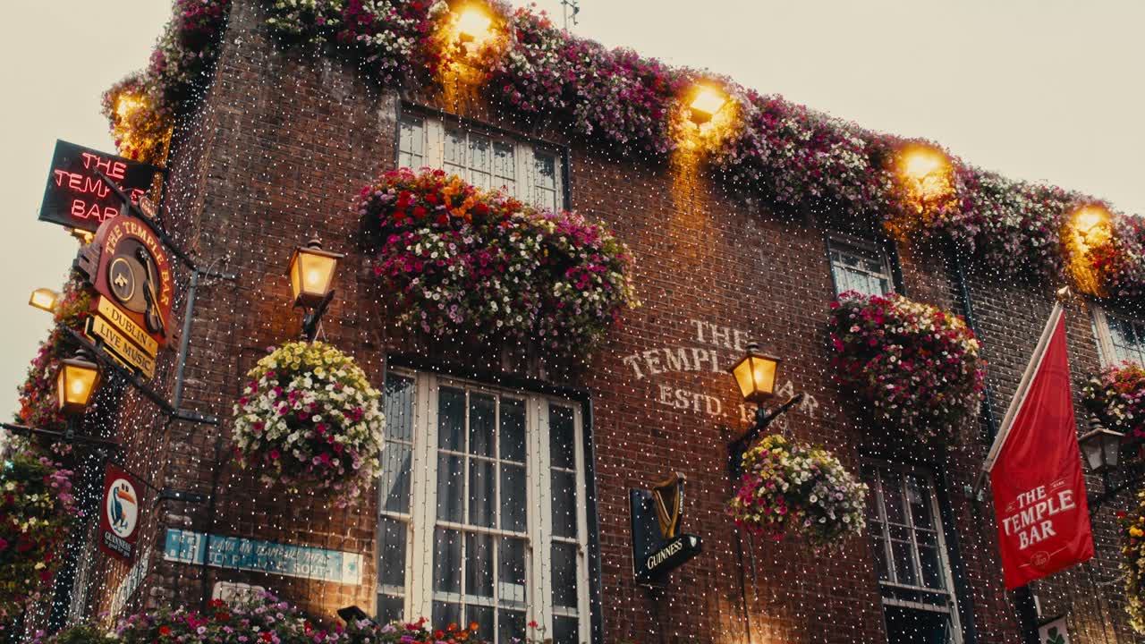 Low-angle shot of The Temple Bar’s brick facade with lights, flowers, and traditional Irish signage - Ireland