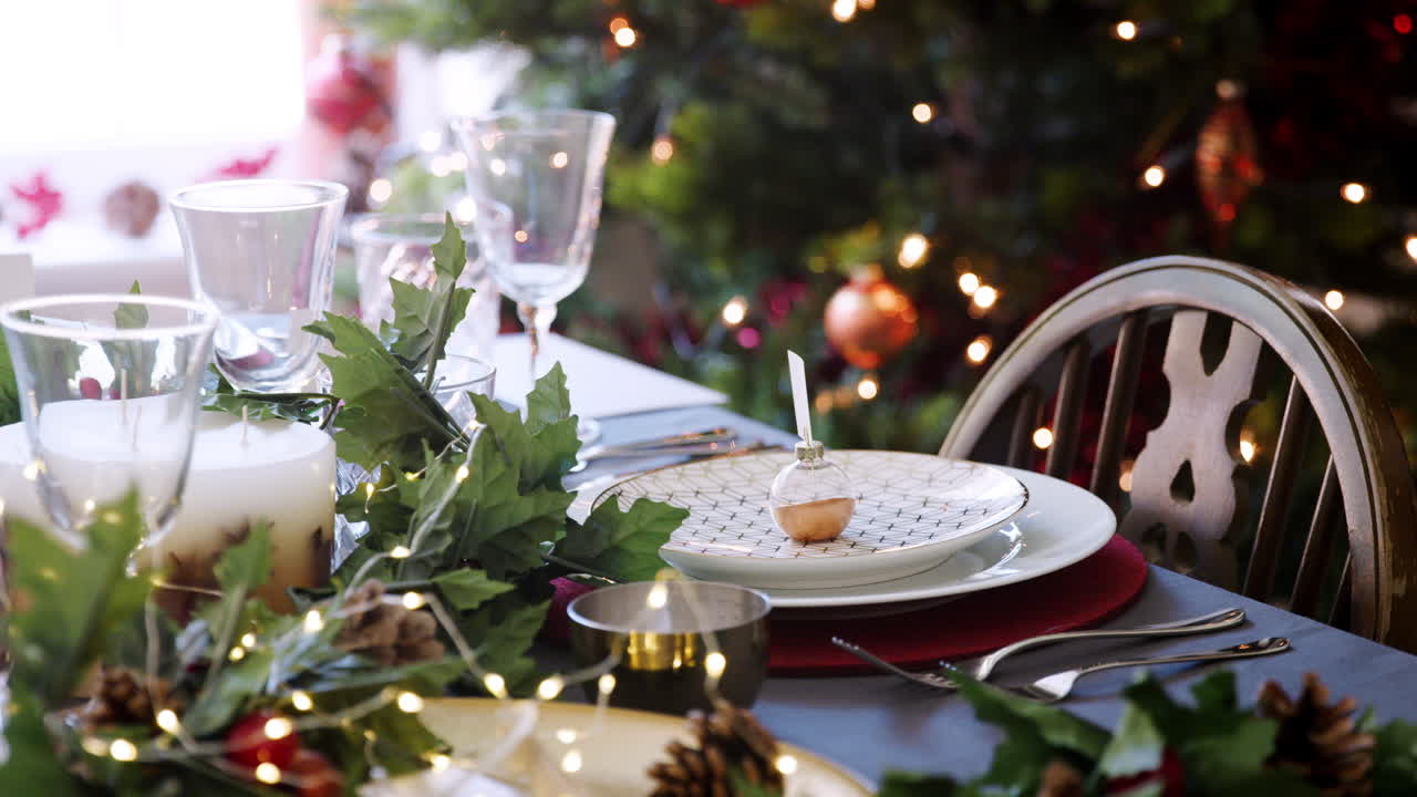 decoración de mesa de navidad con un soporte de tarjeta de nombre de joyas dispuesto en un plato y decoraciones de mesa verdes y rojas, árbol de navidad y luces en el fondo, de cerca