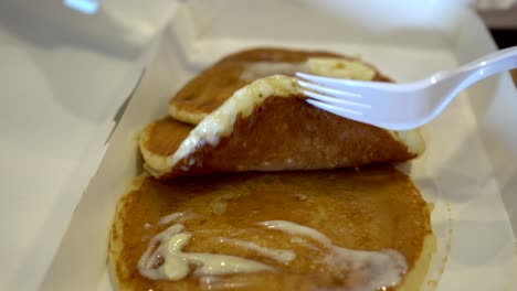 close up of child's hand with knife and fork. the child spreads the cream on the pancake.