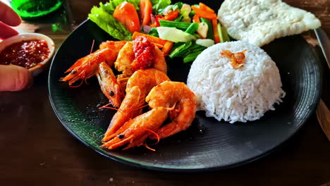 Delicious shrimp served with rice, vegetables, and a side of dipping sauce on a black plate