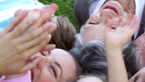 Multi-generation-family-smiling-and-lying-on-ground-in-a-park-waving-up