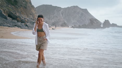 Happy-woman-communicating-telephone-walking-ocean-waves.-Girl-talking-vertical