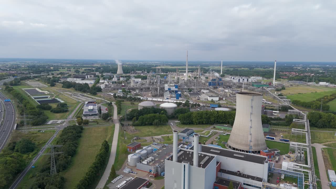 Drone aerial view of a large industrial plant featuring a cooling tower, smokestacks, and surrounding infrastructure