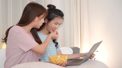 Zwei-Schöne-Mädchen-Essen-Snacks-Und-Popcorn,-Während-Sie-Gemeinsam-Einen-Film-Auf-Dem-Laptop-Im-Schlafzimmer-Anschauen