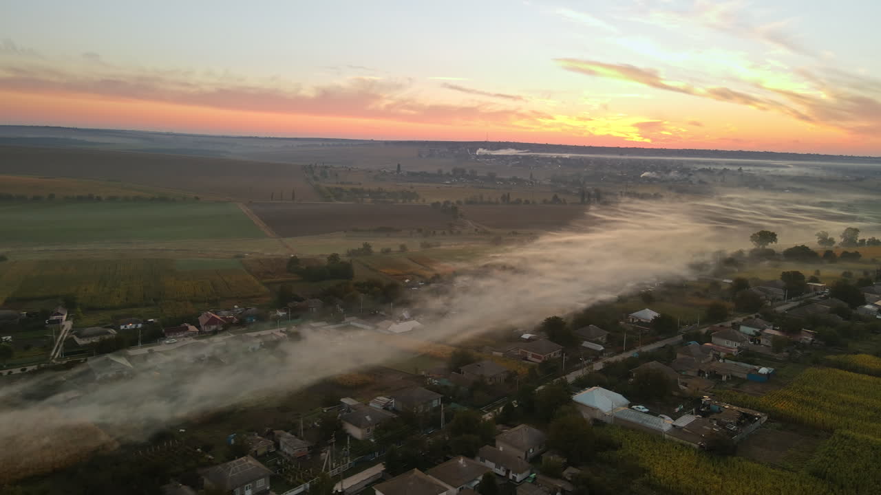 Aerial drone view of village in Moldova at sunset. Few columns of smoke from fires, wide fields
