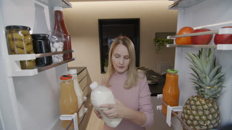 una mujer joven toma una botella de leche del refrigerador