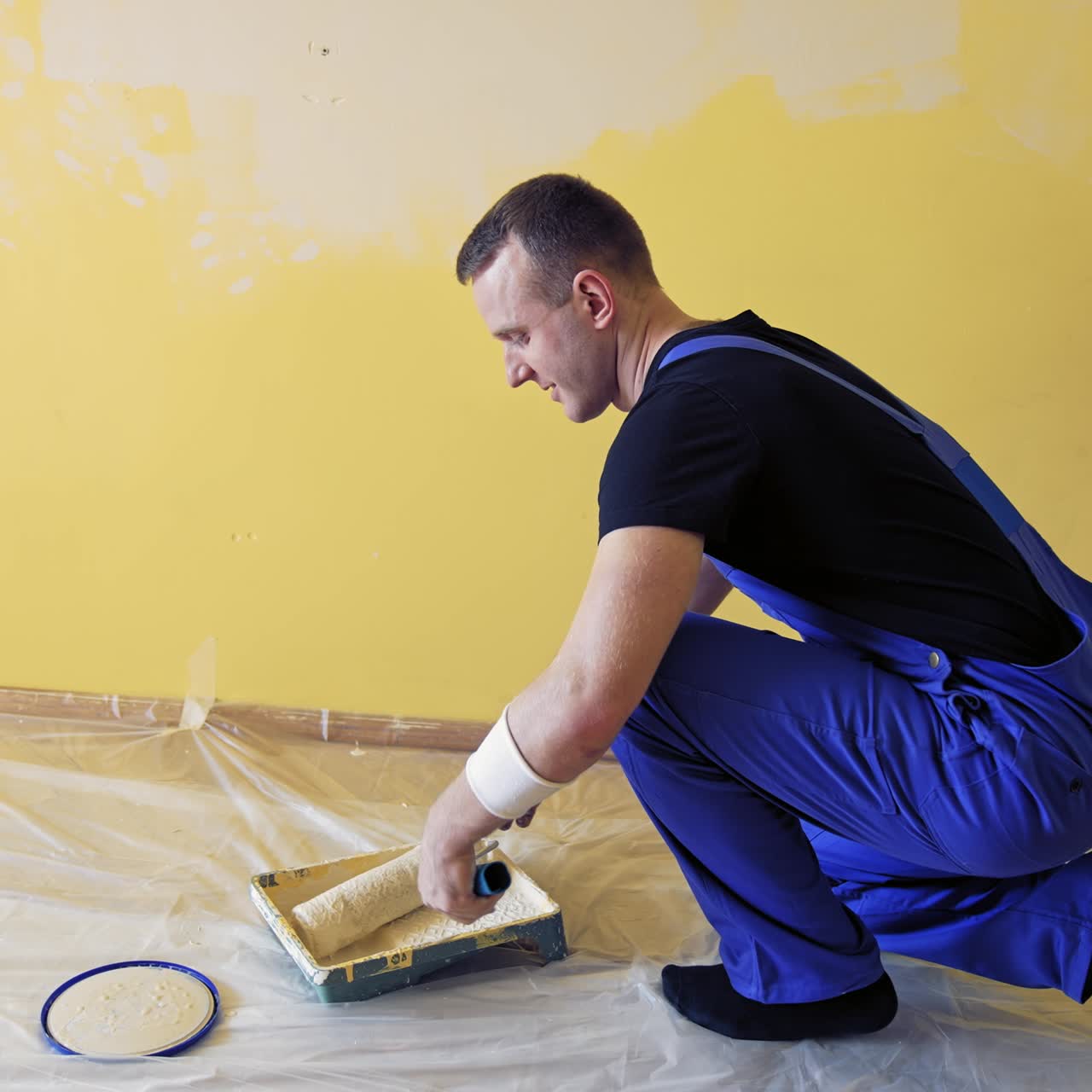 Painter rolling paint roller in color on a tray. Handyman working with a paint roller and having a pain in back. Renovation at home