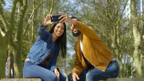 Front-view-of-happy-young-mixed-race-couple-clicking-selfie-with-mobile-phone-in-the-city-4k