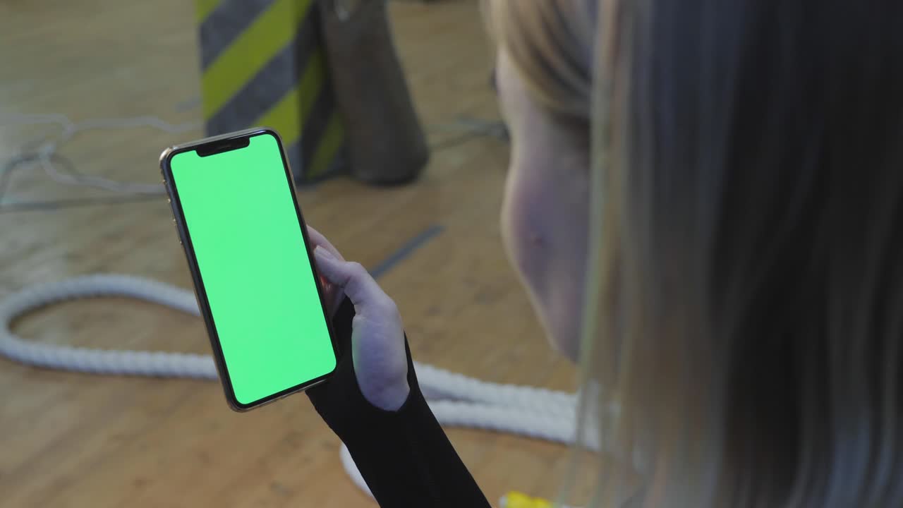 una joven atlética sostiene un teléfono inteligente en la mano, muestra una pantalla chromakey verde, está en el gimnasio