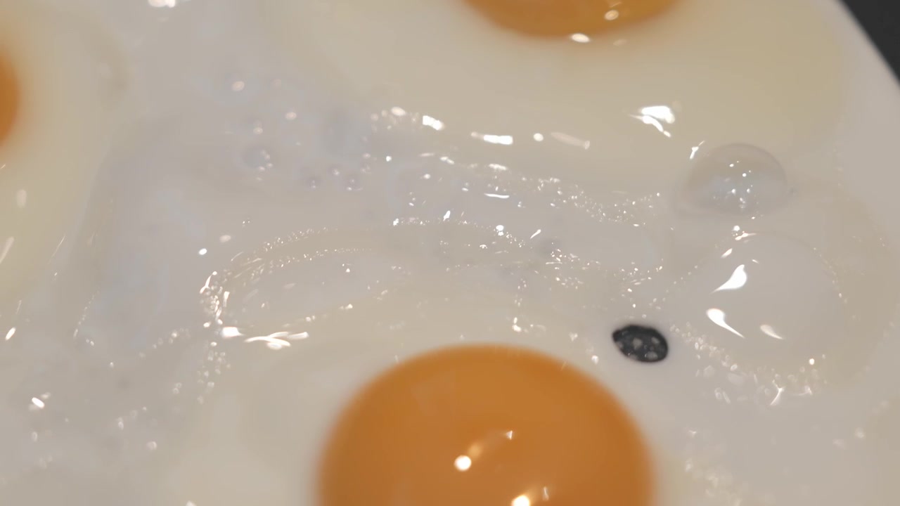 Close-up of a fried egg cooking in a hot pan, capturing sizzling oil, golden edges, and a freshly prepared breakfast scene.