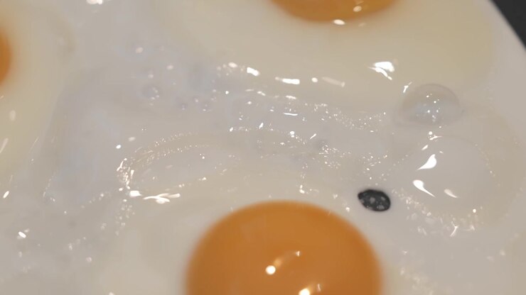 Close-up of a fried egg cooking in a hot pan, capturing sizzling oil, golden edges, and a freshly prepared breakfast scene.